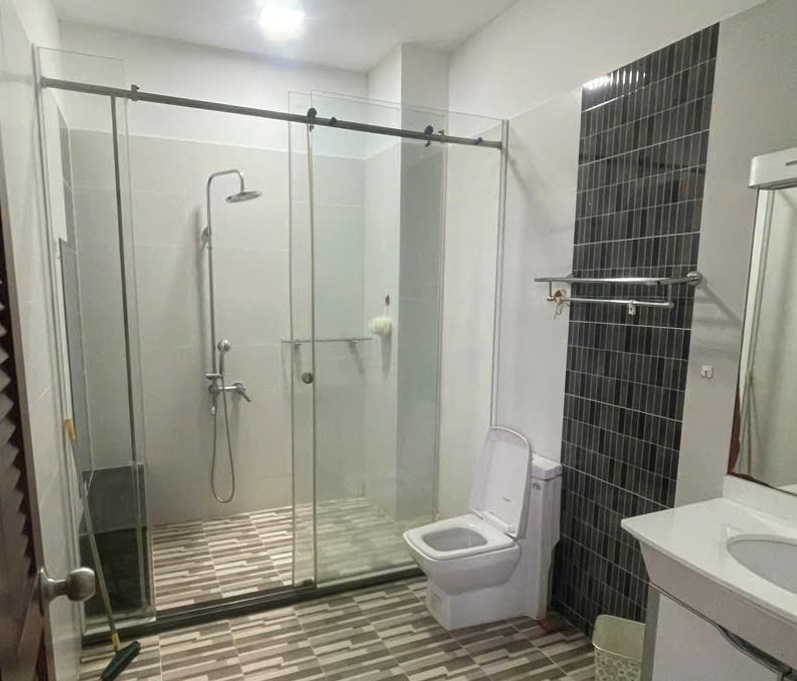 Nhà vệ sinh cũ có vách kính tắm, lavabo và nền gạch vân sọc trước khi cải tạo
